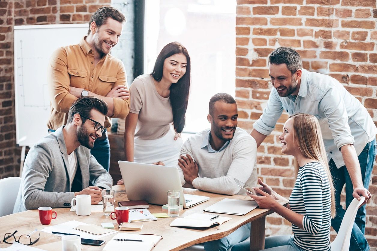 A group of people sitting around a table with a laptop.